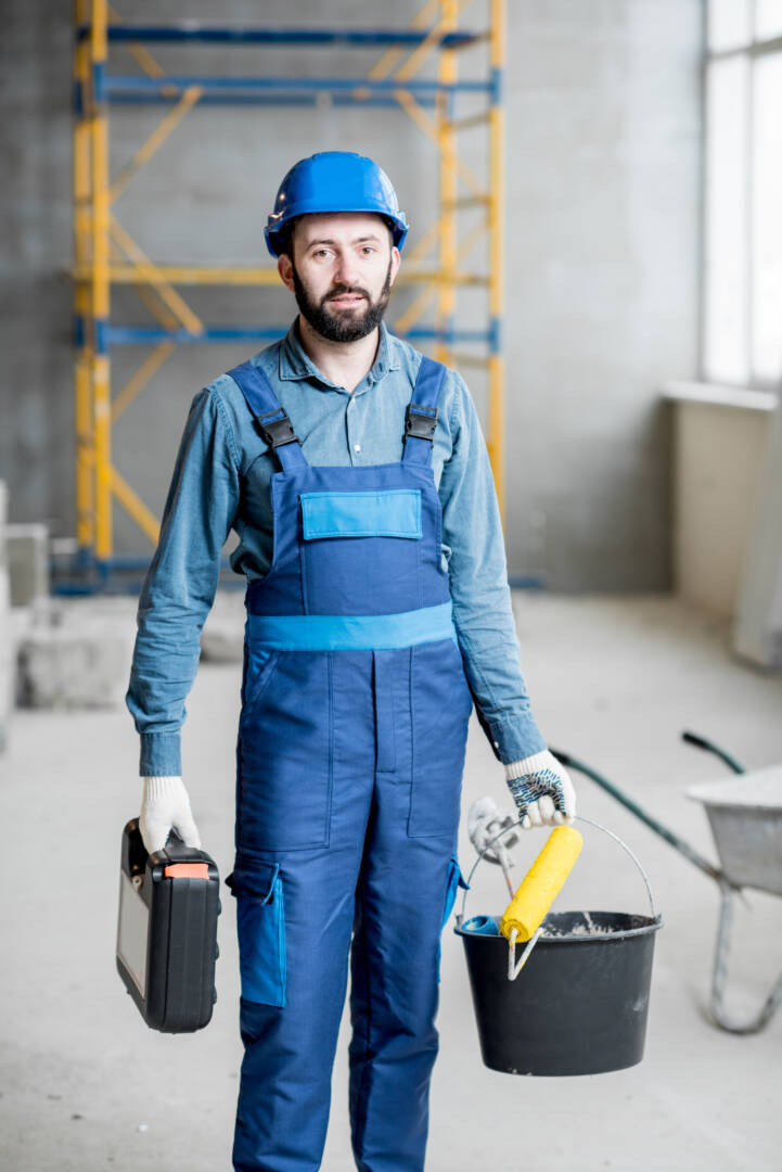 Portrait of a builder in working uniform with protective helmet standing with instruments at the construction site indoors